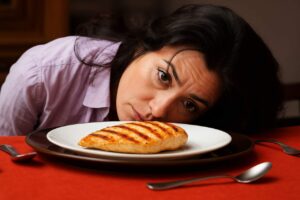 Donna a dieta demoralizzata che guarda il suo petto di pollo alla griglia