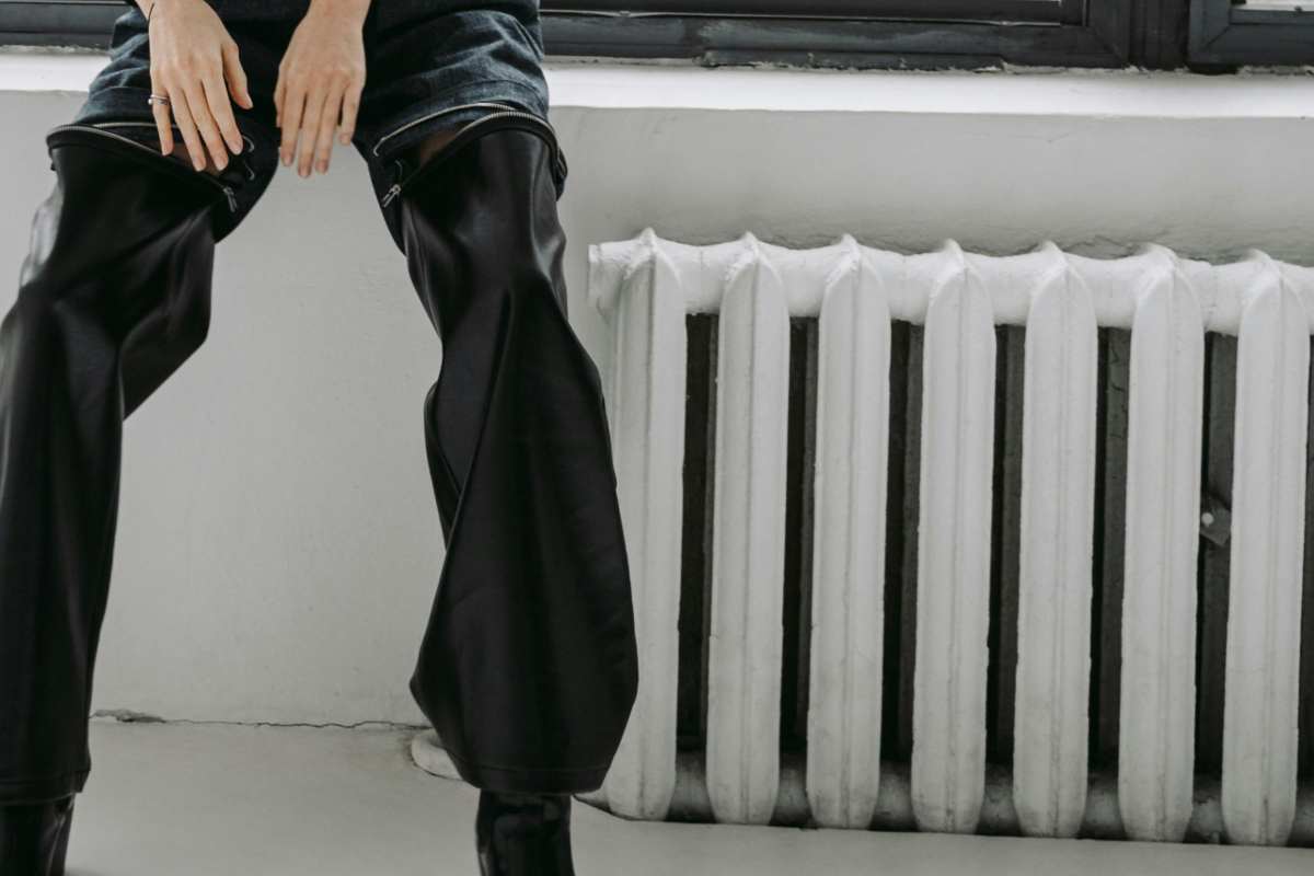 Delle gambe di una donna vicine a un termosifone bianco