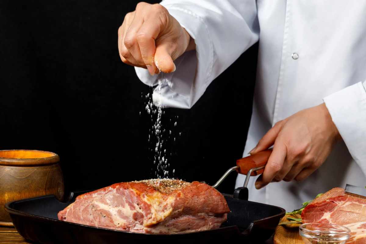 Persona che condisce la carne e la cuoce sul fuoco