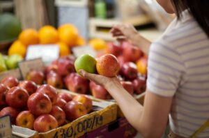 Donna al supermercato con due mele in mano