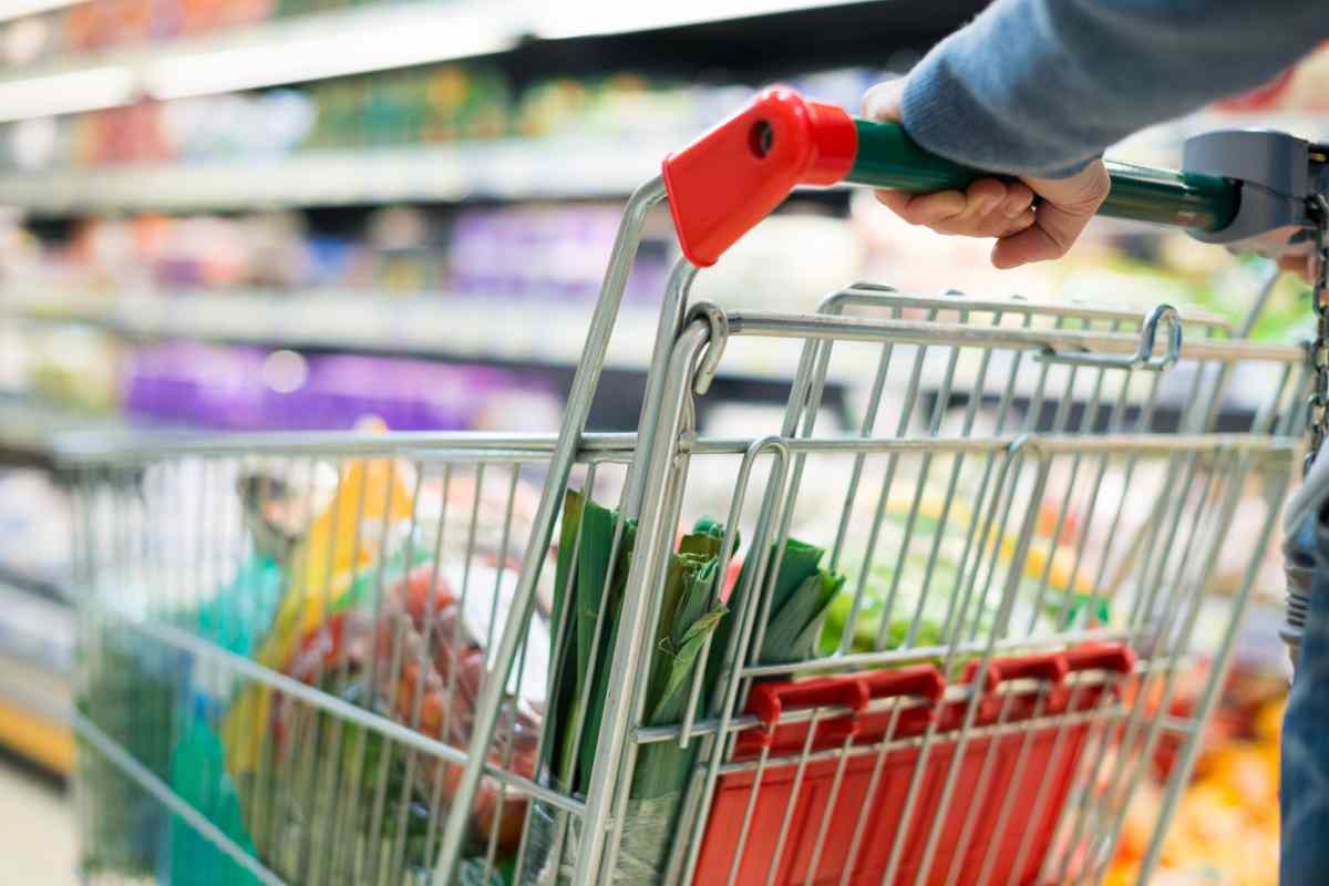 Persona che spinge carrello pieno in un supermercato