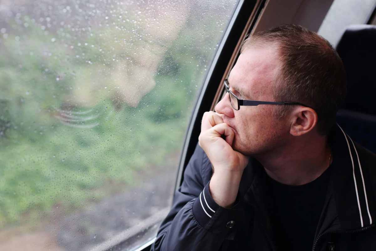 Uomo che guarda la pioggia dal finestrino della macchina