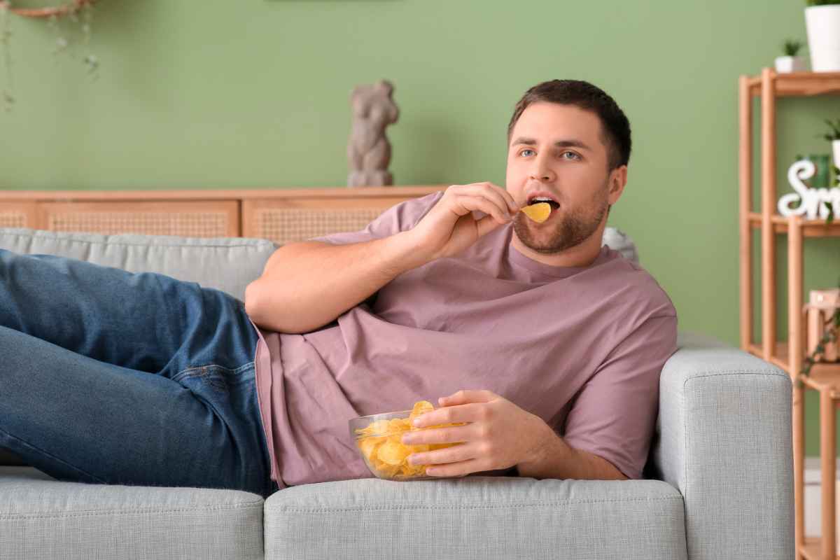 Uomo sdraiato sul divano mentre mangia patatine