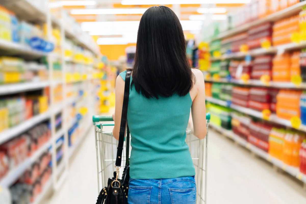 Donna di spalle che cammina in un supermercato con il carrello