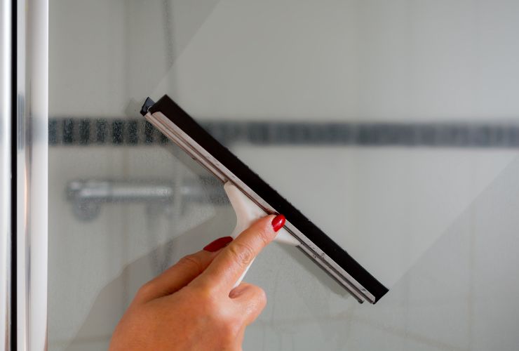 donna che pulisce vetri box doccia