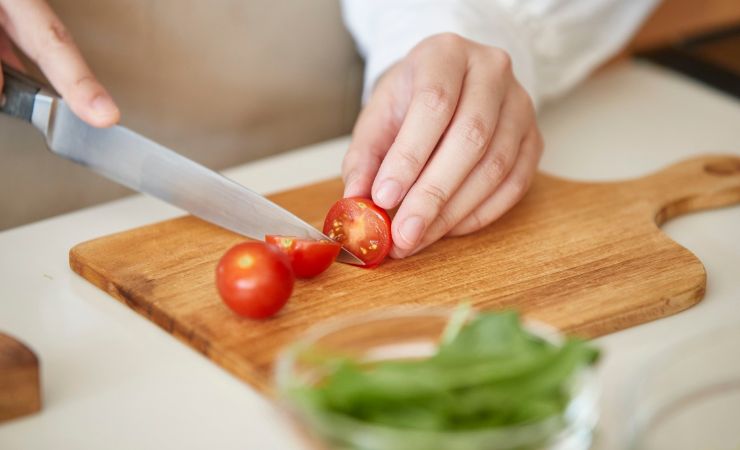 donna che usa tagliere di legno per tagliare pomodori